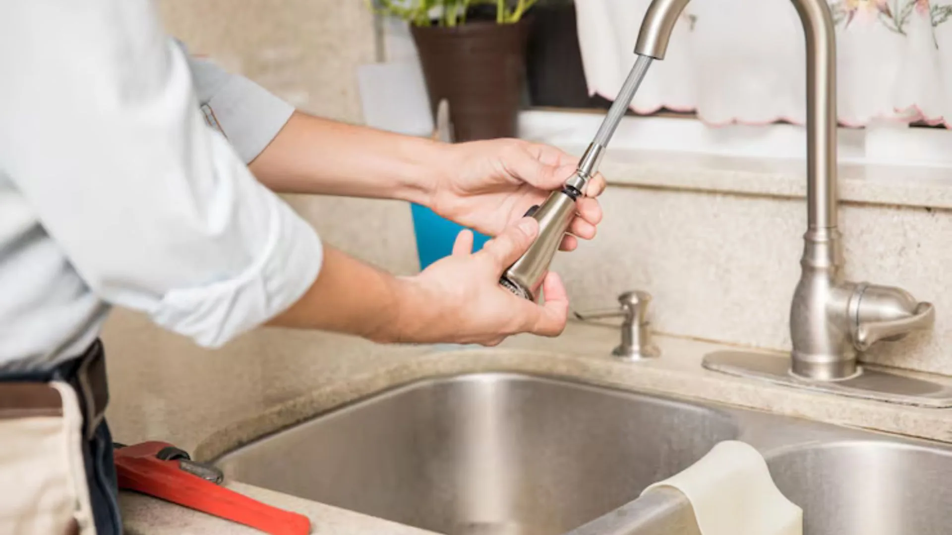 Hands repairing a kitchen faucet spout above a stainless steel sink